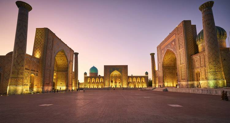 Les grandes madrasas de la place du Régistan brillant au crépuscule avec des visiteurs se promenant sur la plaza.