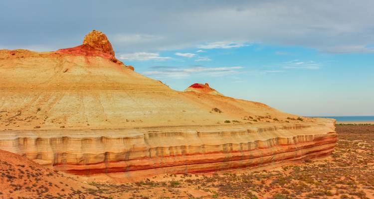Falaises désertiques stratifiées aux tons chauds rouge et beige sous un ciel bleu partiellement nuageux.