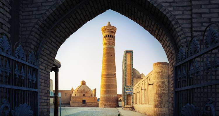 Minaret historique et cour de mosquée encadrés par une porte voûtée à l'heure dorée.