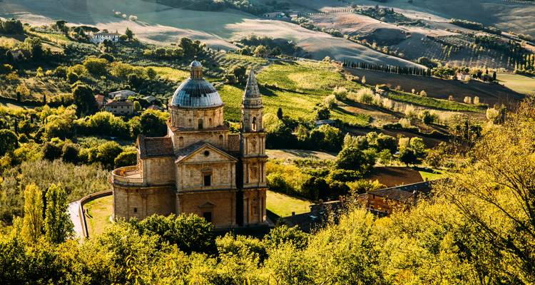 San Biagio Kirche eingebettet zwischen goldenen Feldern und sanften Hügeln des Val d'Orcia in warmem Licht.