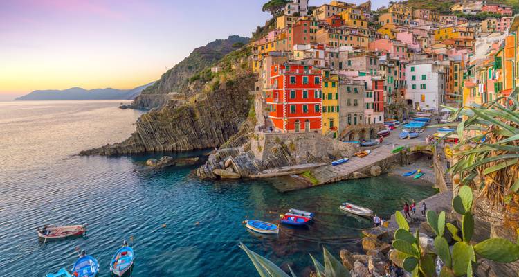 Luminoso pueblo en el acantilado de Riomaggiore con casas coloridas sobre una cala serena al atardecer.