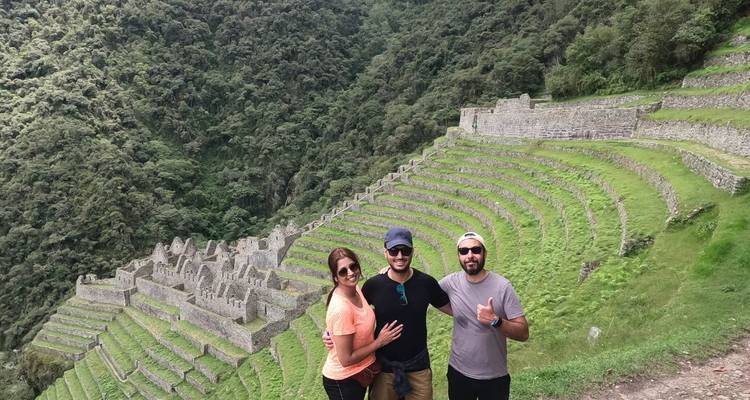 Trois voyageurs sourient devant d'anciennes terrasses de pierre le long du Chemin de l'Inca.