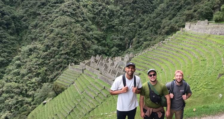 Trois randonneurs avec des sacs à dos se tiennent devant des terrasses vertes escarpées dans les Andes.