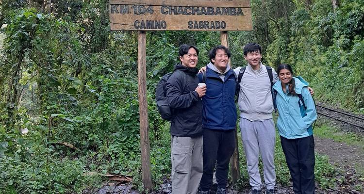 Un groupe se tient à côté d'un panneau en bois "KM 104 Chachabamba Camino Sagrado" dans une forêt luxuriante.