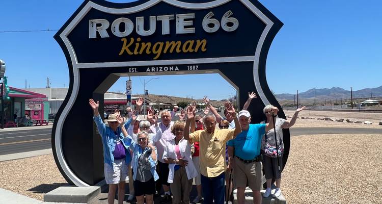 Groupe de touristes heureux posant sous un grand panneau bouclier Route 66 Kingman dans le soleil du désert de l'Arizona.