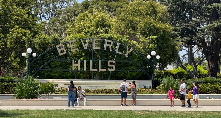 Los visitantes posan bajo el famoso letrero de Beverly Hills en un parque urbano frondoso.