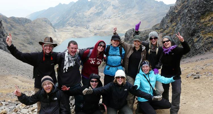 Groupe de randonneurs joyeux posant les bras levés sur un col rocheux surplombant un lac glaciaire