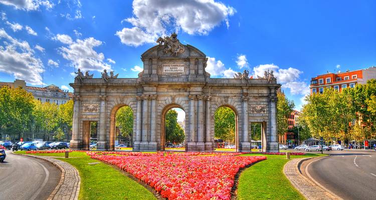 Triumphbogen Puerta de Alcalá, umrahmt von farbenfrohen Blumenbeeten an einem hellen Tag in Madrid.
