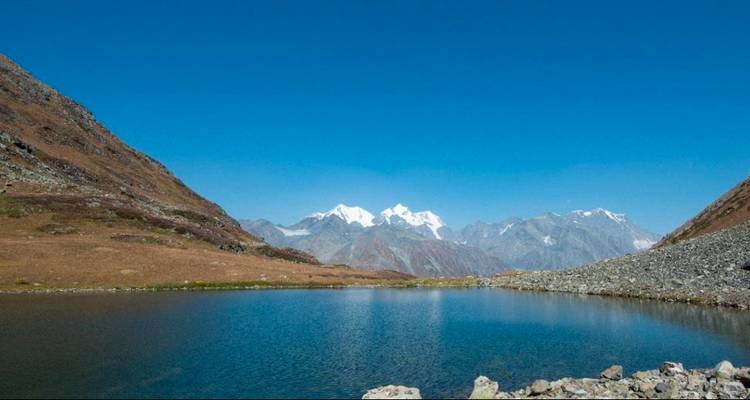 Hooggelegen alpenmeer dat met sneeuw bedekte toppen weerkaatst onder een wolkenloze diepblauwe hemel.