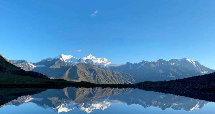 Kristalhelder bergmeer dat de gekartelde besneeuwde bergketen bij dageraad perfect weerkaatst.