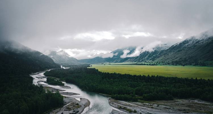 Sombere luchtfoto van kronkelende rivier en groene vallei onder laaghangende wolken en mist.