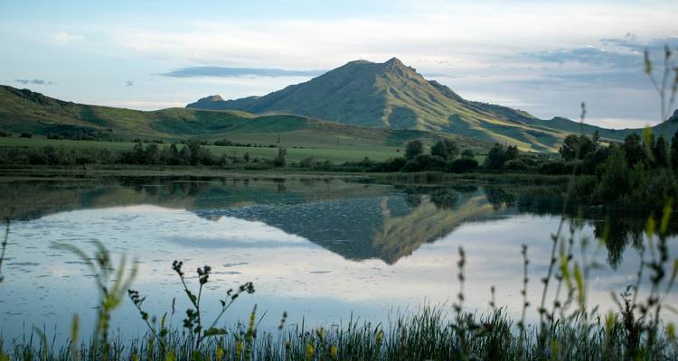 Paysage montagneux serein reflété dans un lac immobile avec des collines vertes et des nuages doux.