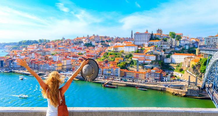 Mujer joven levantando los brazos con alegría contemplando la colorida ribera de Oporto y el Puente Dom Luís I.
