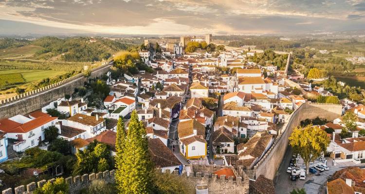 Vista aérea del pueblo medieval amurallado de Óbidos con casas encaladas y techos de terracota al atardecer.