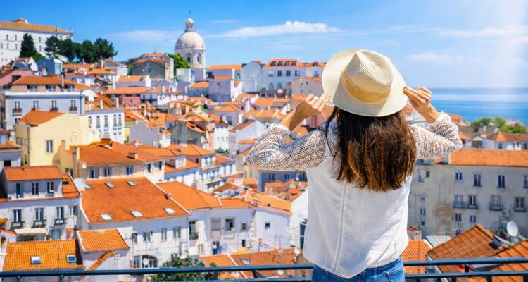 Viajera con sombrero de paja admirando el distrito de Alfama de Lisboa y el telón de fondo del Tajo.