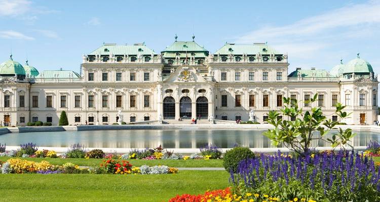 Het sierlijke barokke Belvedere Palace in Wenen met kleurrijke tuinen en vijver met spiegeling onder een blauwe lucht.