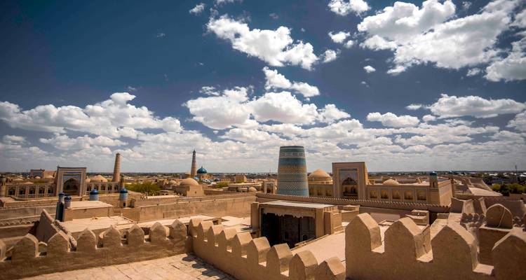 Point de vue élevé sur la ville fortifiée de Khiva montrant les minarets, dômes et remparts fortifiés sous des nuages épars.