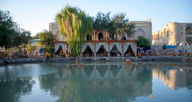 Chaikhana traditionnel au bord du lac avec terrasses à rideaux se reflétant dans l'étang immobile d'une place de vieille ville sous la douce lumière de l'après-midi.