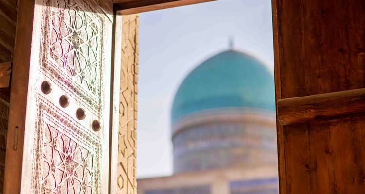 Entrée en bois sculpté brillant dans la lumière du soleil avec un dôme turquoise doucement flou encadré au loin.