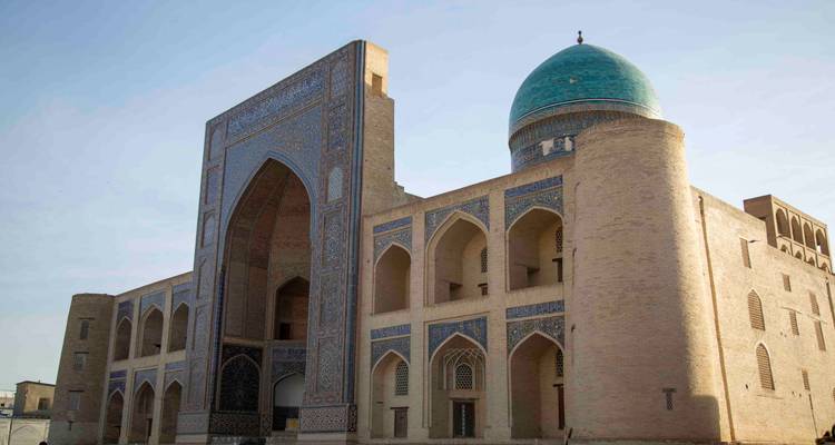 Grande madrasah en brique couronnée d'un dôme turquoise éclatant et de portails décorés sous un ciel bleu clair.
