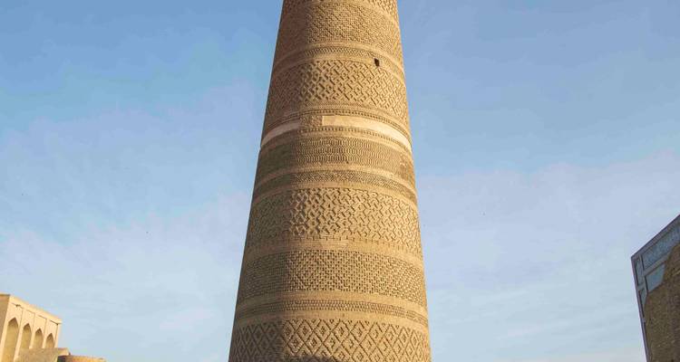 Minaret en briques à motifs s'élevant contre un ciel bleu pâle, vu depuis sa base.
