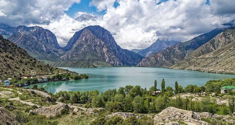 Turkooisalpien meer omgeven door steile beboste hellingen en ruige grijze bergen onder een gedeeltelijk bewolkte hemel.