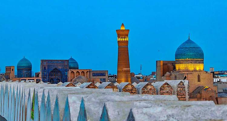 Avondsilhouet met verlichte minaret en blauwe koepels die boven de oude stadsmuren uitsteken tijdens het blauwe uur.