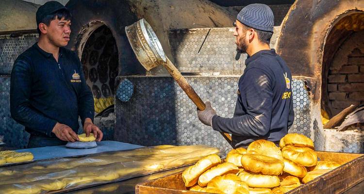 Twee bakkers werken bij een traditionele kleioven en kneden en bakken gouden ronde broden.