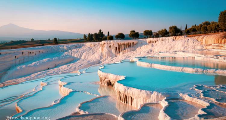 Las terrazas de travertino blanco y las piscinas turquesas de Pamukkale caen en cascada por una ladera bajo cielos azules.