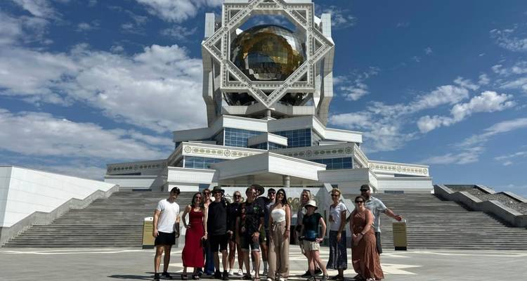 Un grupo de turistas posa en amplias escaleras frente a un edificio futurista blanco con una esfera dorada en Asjabad.