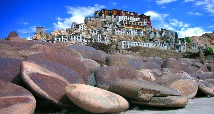 Froschperspektive des Thiksey-Klosters, das auf einer felsigen Hügelkuppe thront, mit großen runden Felsbrocken, die den Vordergrund dominieren, und einem tiefblauen Himalaya-Himmel darüber.
