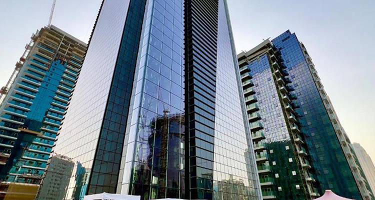 Rascacielos moderno de cristal flanqueado por otros edificios de gran altura contra un cielo despejado.