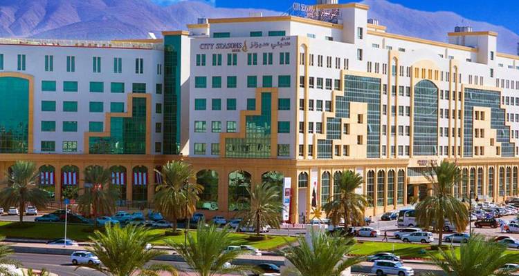 Gran complejo hotelero moderno con montañas de fondo y bulevar bordeado de palmeras.