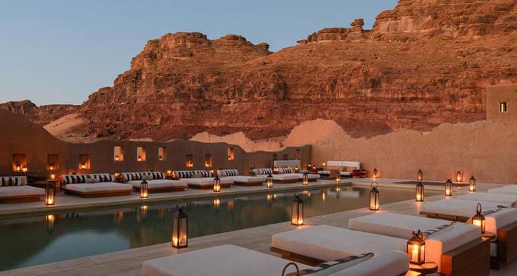 Piscina boutique estilo desértico bordeada de faroles entre espectaculares acantilados rojos al atardecer.