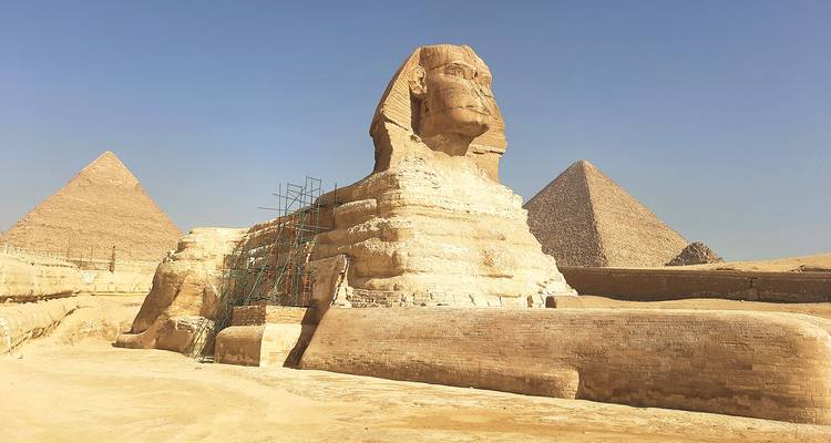 Vista lateral de la Gran Esfinge con dos pirámides elevándose detrás de ella en un día brumoso