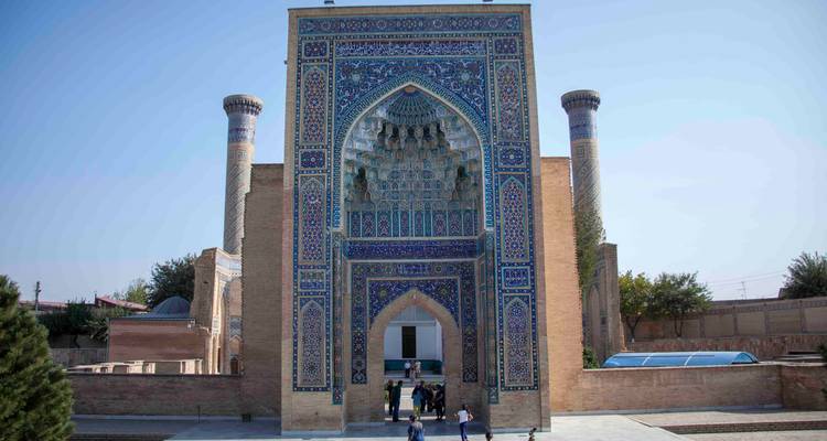 Grand portail de mosquée richement carrelé avec deux minarets jumeaux et quelques touristes debout à la base.