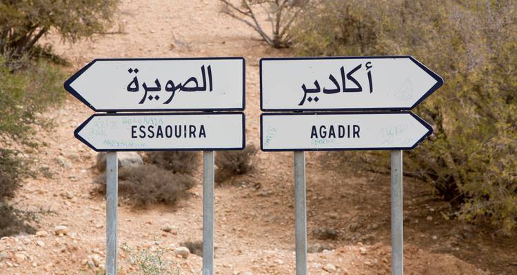 Tweetalige verkeersborden wijzen de richting naar Essaouira en Agadir te midden van een ruig woestijnlandschap.
