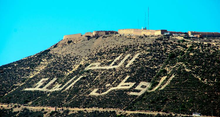 Arabisch motto uitgepikt in witte stenen siert de heuvelzijde onder de oude kasbah-muren van Agadir.