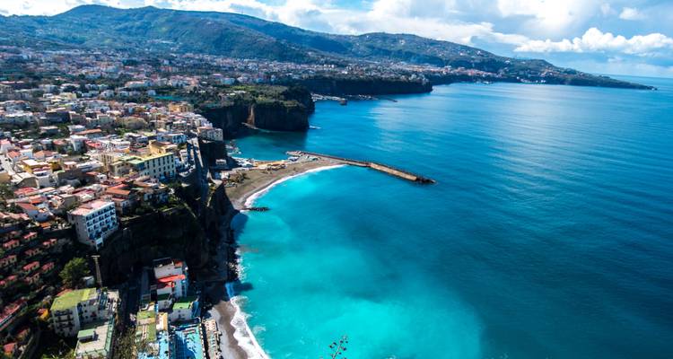 Hoge luchtfoto van Sorrento's uitgestrekte kustlijn met diepe turquoise baaien en verre heuvels.