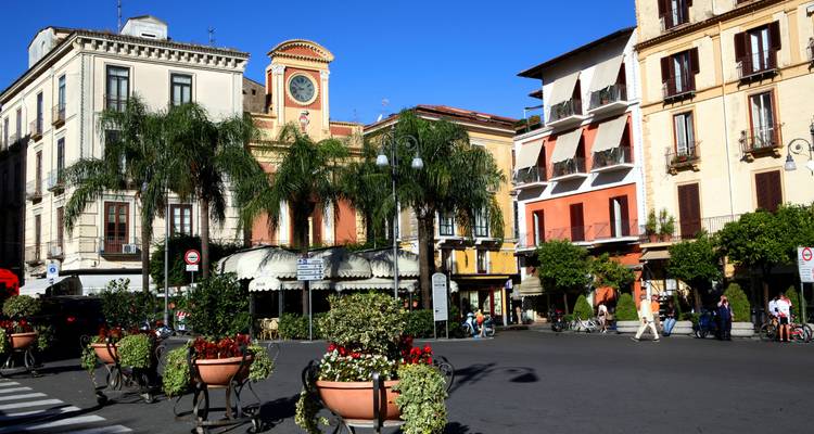 Bruisende Piazza Tasso in Sorrento omzoomd met palmbomen, cafés en kleurrijke gevels onder een heldere hemel.