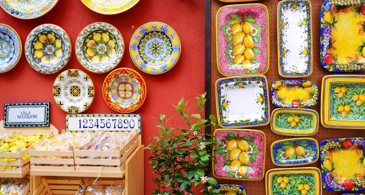 Kleurrijke handgeschilderde keramische borden en tegels tentoongesteld op een levendige rode muur in Sorrento.