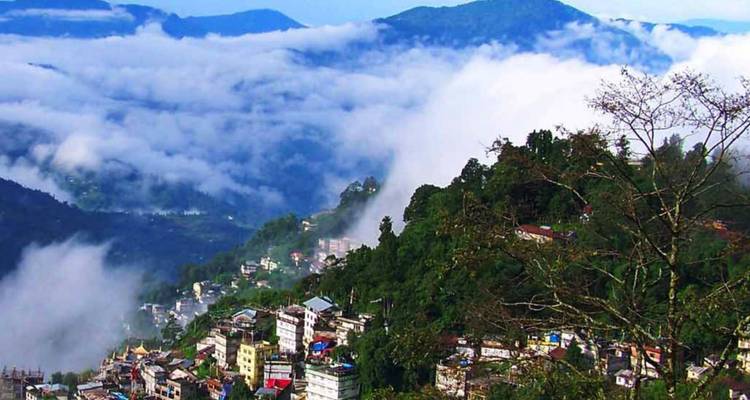 Nebel treibt durch üppig grüne Täler, während eine Bergstadt unter rollenden Wolken hervorlugt.