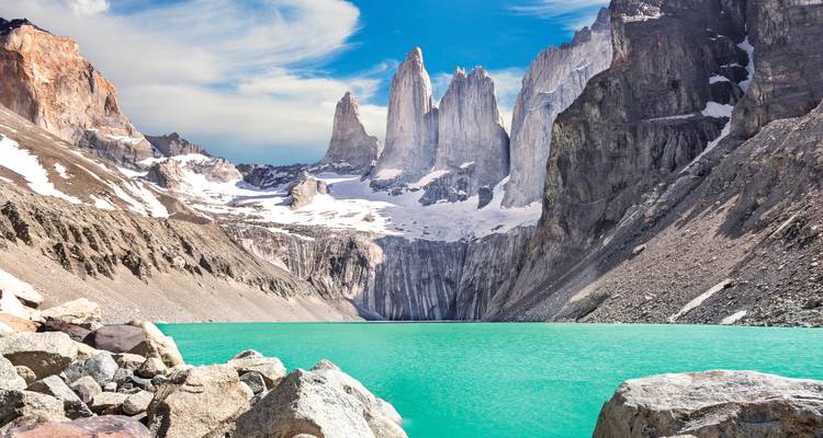 Iconische granieten torens van Torres del Paine die oprijzen boven een levendig turkoois gletsjermeer en rotsachtige kustlijn.