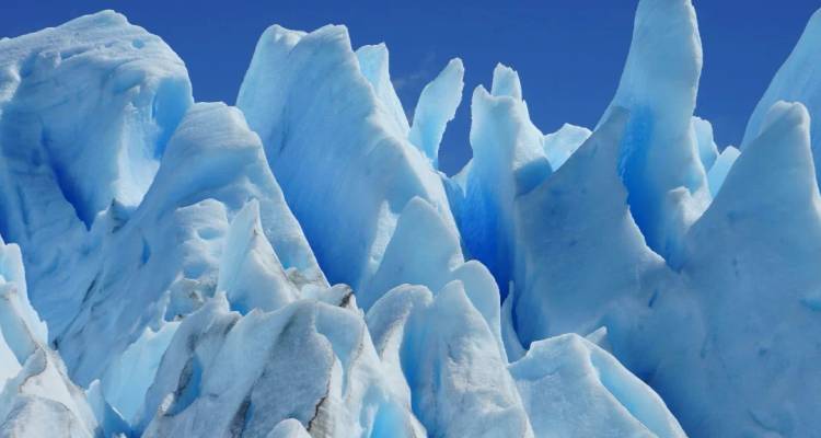 Gros plan sur les pics de glace bleus dentelés d'un glacier massif sur un ciel dégagé.