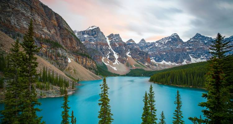 Turquoise Moraine Lake framed by tall pines and towering snow-dusted peaks in Banff National Park.
