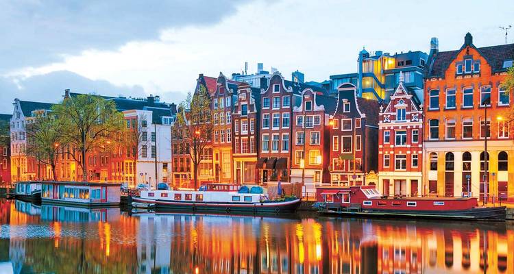 Escena nocturna de canal con casas de tejados a dos aguas brillantemente iluminadas reflejándose en el agua en Ámsterdam.