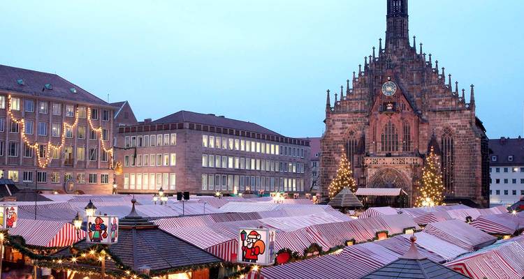 Vista del crepúsculo de puestos de mercado festivos con la Frauenkirche iluminada en Núremberg.