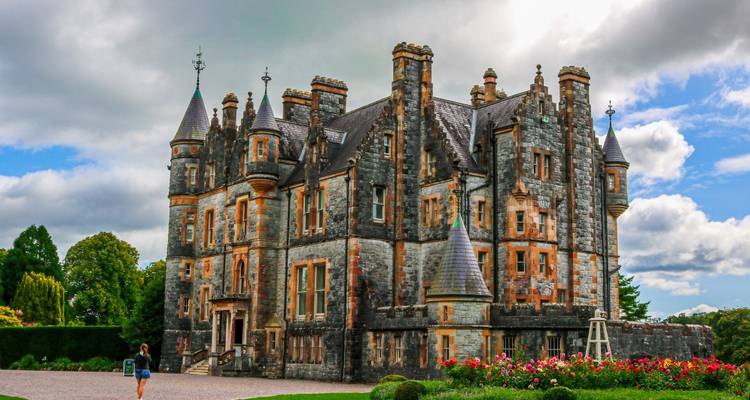 Impresionante castillo de la era victoriana con torreones, jardines bien cuidados y un visitante solitario paseando por los terrenos.