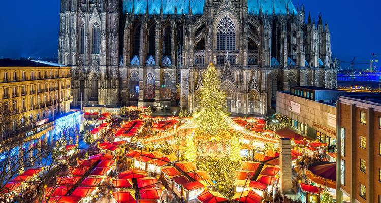 Feestelijke kerstmarkt met gloeiende lichten onder de torenhoge Keulse Dom in de nacht.