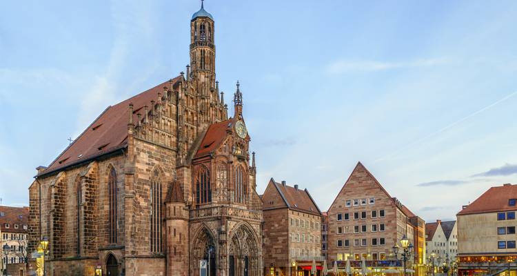 Iglesia gótica Frauenkirche en la plaza Hauptmarkt rodeada de edificios históricos en Núremberg al atardecer.